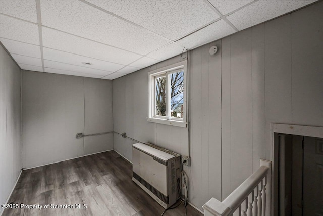 basement with heating unit, a drop ceiling, and wood finished floors