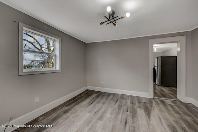 spare room with an inviting chandelier, baseboards, wood finished floors, and ornamental molding