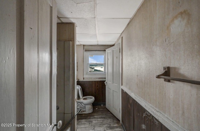 bathroom with a paneled ceiling, wood walls, toilet, and wood finished floors