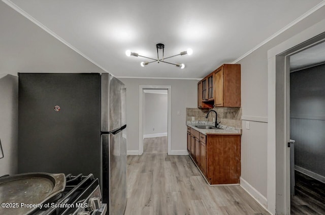 kitchen featuring tasteful backsplash, brown cabinets, freestanding refrigerator, light wood-type flooring, and a sink