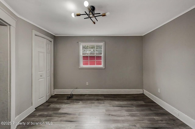 unfurnished bedroom with a closet, an inviting chandelier, ornamental molding, wood finished floors, and baseboards