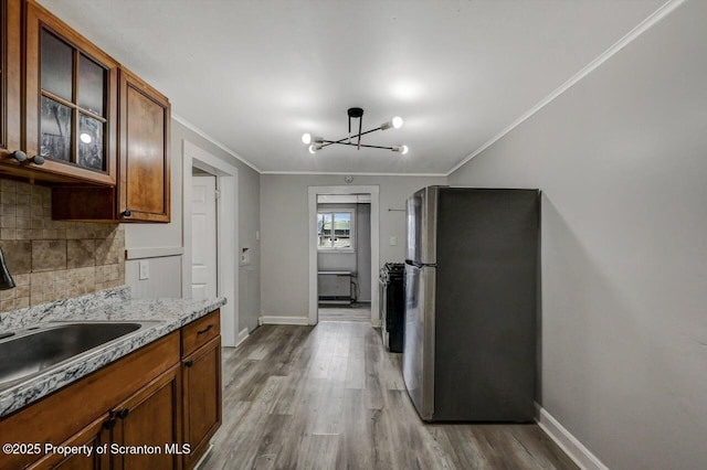 kitchen featuring wood finished floors, baseboards, freestanding refrigerator, decorative backsplash, and crown molding