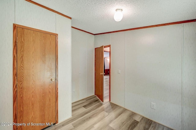 empty room featuring a textured ceiling, light hardwood / wood-style floors, and crown molding