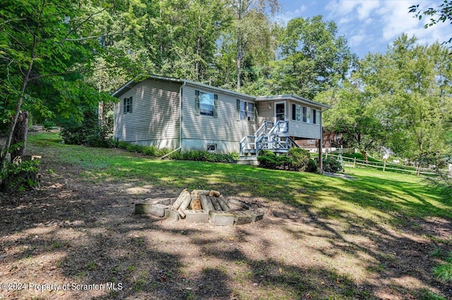 back of house featuring a fire pit, a deck, and a lawn