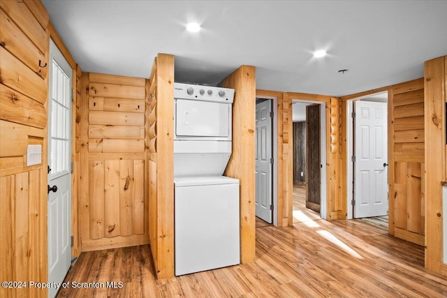 laundry room with rustic walls, light hardwood / wood-style flooring, and stacked washer and clothes dryer