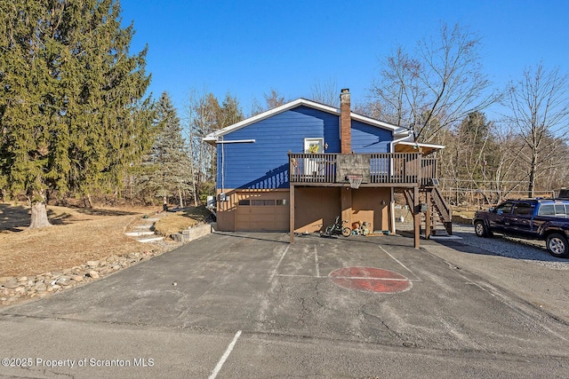 chalet / cabin with stairway, an attached garage, a chimney, and aphalt driveway