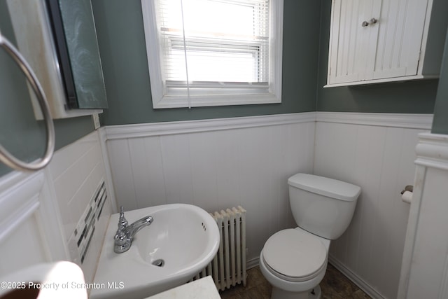 half bath featuring a sink, toilet, radiator heating unit, and wainscoting