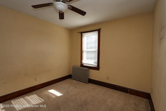 spare room with baseboards, light carpet, ceiling fan, and radiator heating unit