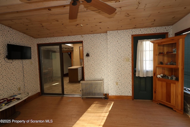 empty room featuring wallpapered walls, radiator heating unit, a ceiling fan, and light wood-type flooring