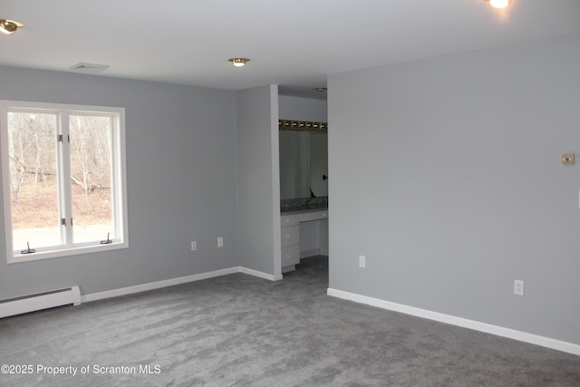 carpeted spare room with a baseboard heating unit, visible vents, baseboards, and built in desk