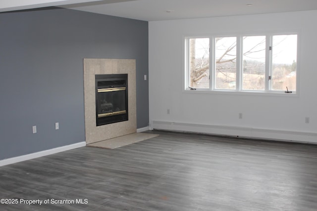 unfurnished living room with a healthy amount of sunlight, a fireplace, wood finished floors, and a baseboard radiator