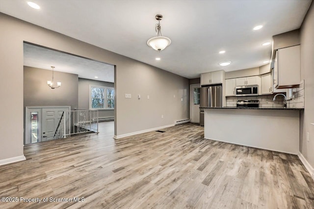 kitchen with appliances with stainless steel finishes, light wood-type flooring, backsplash, pendant lighting, and white cabinetry