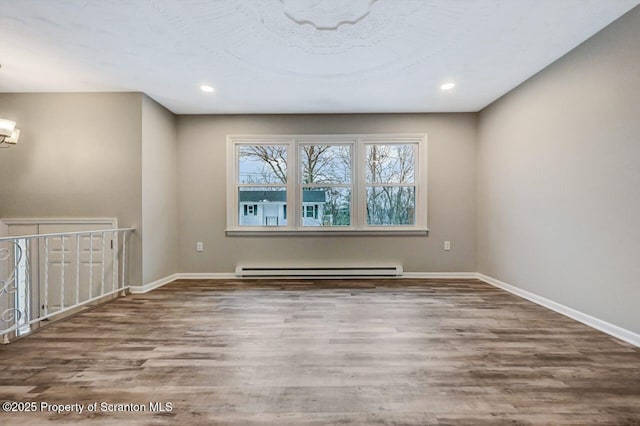 unfurnished room featuring baseboard heating, an AC wall unit, a notable chandelier, and hardwood / wood-style flooring