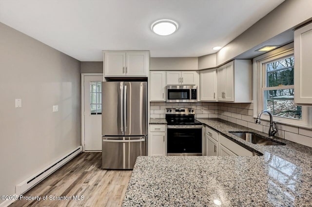 kitchen with light stone counters, sink, baseboard heating, and stainless steel appliances