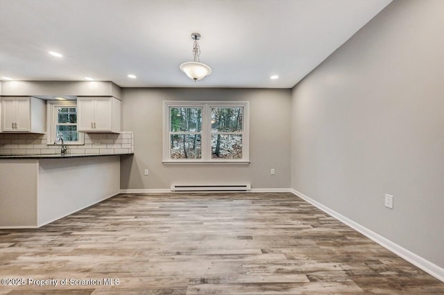 kitchen with a baseboard heating unit, backsplash, pendant lighting, white cabinets, and light wood-type flooring