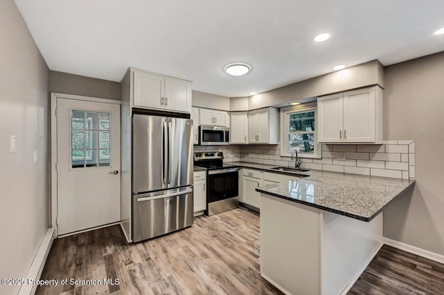 kitchen featuring kitchen peninsula, stainless steel appliances, sink, dark stone countertops, and white cabinetry