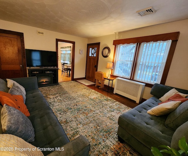 living room featuring visible vents, baseboards, radiator, and wood finished floors