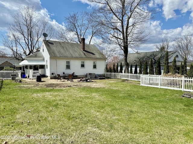 rear view of house with a chimney, a fenced backyard, and a yard