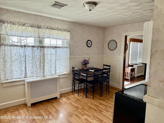 dining space with radiator, wood finished floors, wainscoting, and visible vents