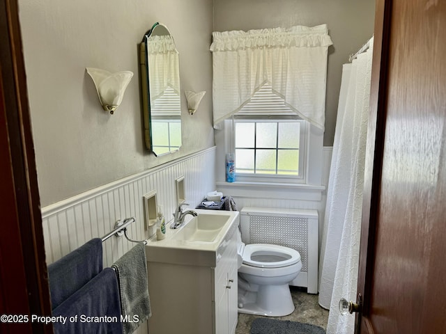 full bathroom featuring toilet, radiator, vanity, and wainscoting