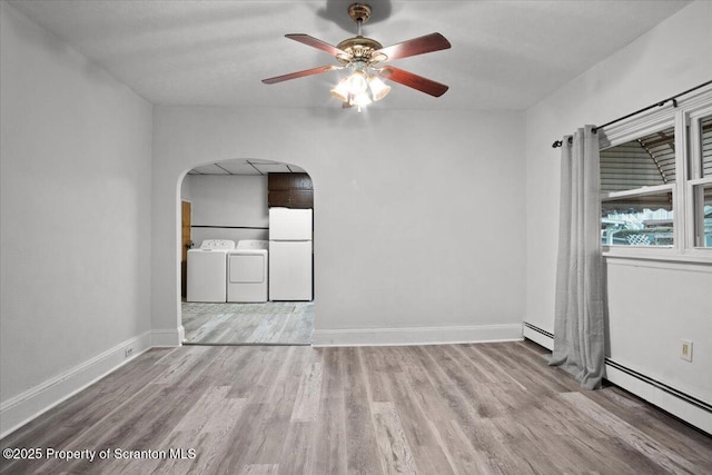 empty room with arched walkways, baseboard heating, washer and dryer, and ceiling fan