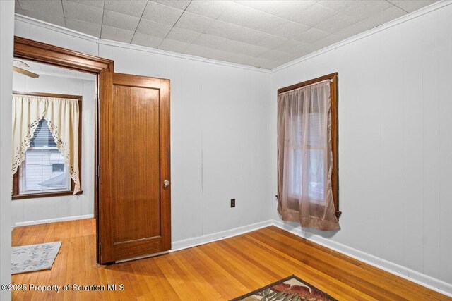 empty room with baseboards, crown molding, and wood finished floors