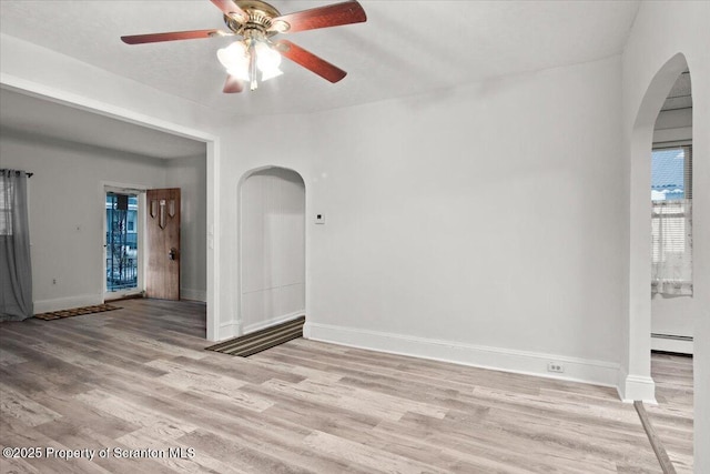spare room featuring ceiling fan, light wood-style floors, baseboards, and arched walkways