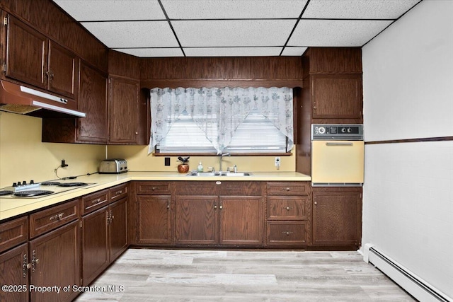 kitchen with a drop ceiling, a sink, a baseboard heating unit, white appliances, and under cabinet range hood