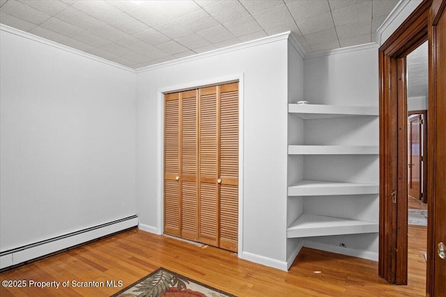 unfurnished bedroom featuring a baseboard radiator, a closet, crown molding, and wood finished floors