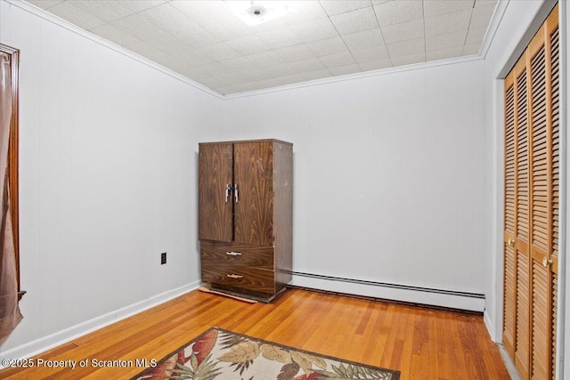 unfurnished bedroom with crown molding, a closet, baseboard heating, and light wood-type flooring