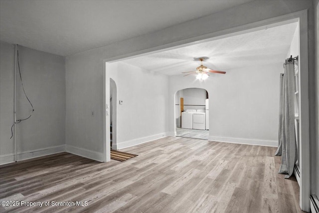 unfurnished living room featuring arched walkways, separate washer and dryer, a ceiling fan, and wood finished floors