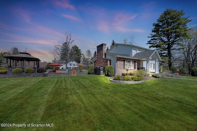 property exterior at dusk with a gazebo and a lawn