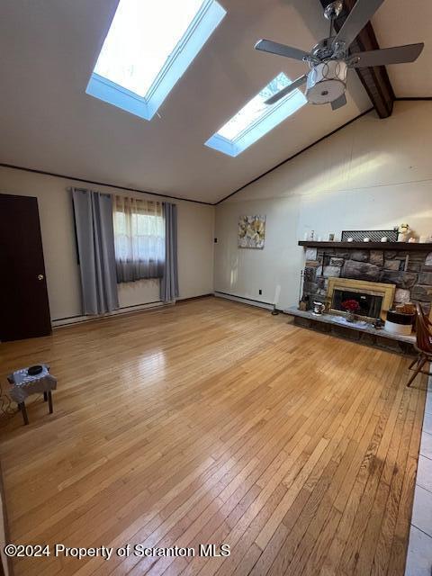 unfurnished living room with lofted ceiling with skylight, ceiling fan, a baseboard heating unit, light hardwood / wood-style flooring, and a stone fireplace