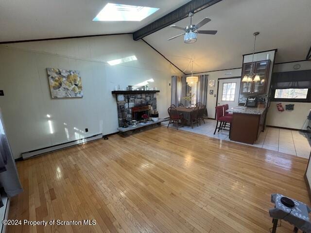 living room featuring light wood-type flooring, lofted ceiling with skylight, ceiling fan, a baseboard radiator, and a stone fireplace