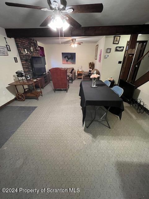 carpeted dining room featuring ceiling fan and beamed ceiling