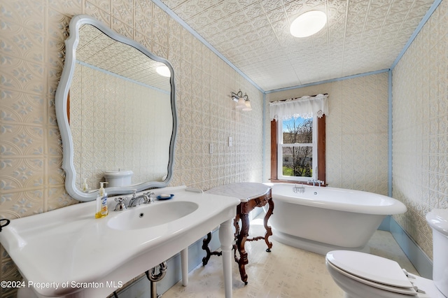 bathroom featuring a washtub, toilet, crown molding, and sink