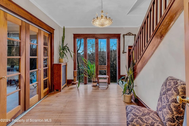 foyer with a chandelier, light wood-type flooring, ornamental molding, and french doors