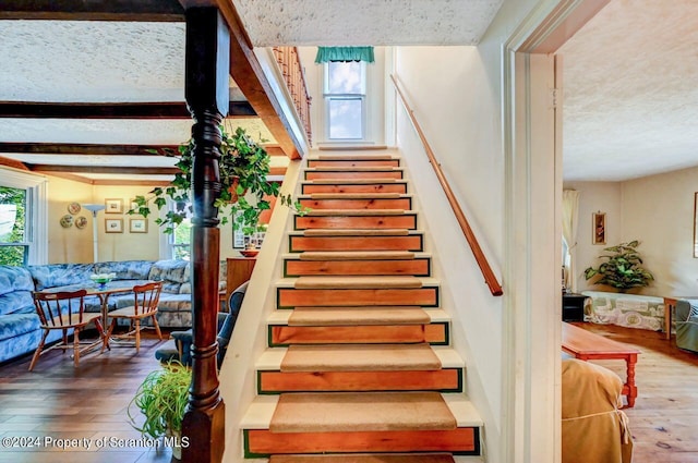 stairway featuring beamed ceiling, wood-type flooring, and a textured ceiling