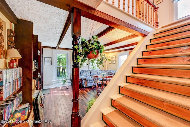 stairway featuring beam ceiling, a textured ceiling, and hardwood / wood-style flooring