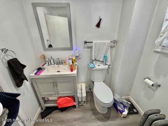 half bathroom with baseboards, vanity, toilet, and wood finished floors