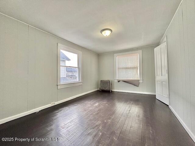 empty room with radiator, baseboards, and wood finished floors