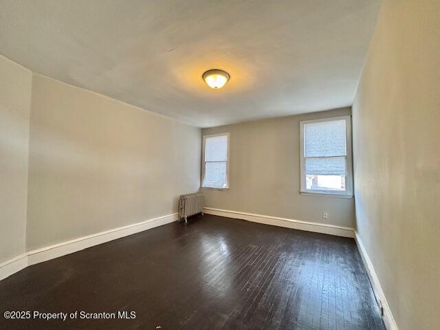 unfurnished room with dark wood-style flooring, baseboards, and radiator heating unit