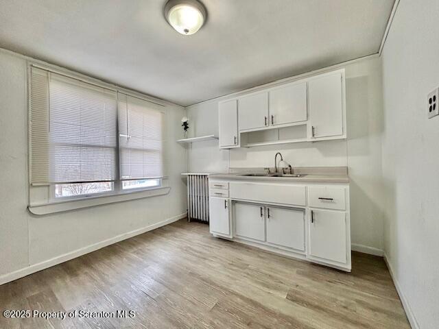 kitchen with open shelves, radiator heating unit, white cabinets, a sink, and light wood-type flooring