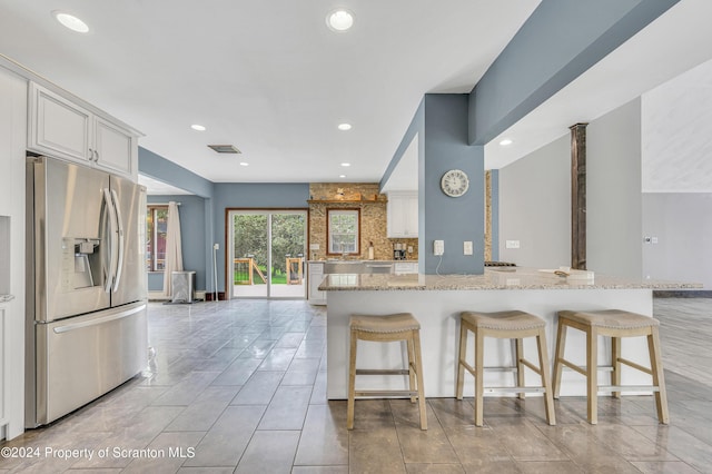 kitchen featuring backsplash, white cabinets, light stone countertops, stainless steel fridge with ice dispenser, and a breakfast bar area