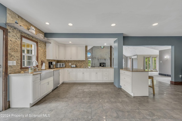 kitchen with stainless steel dishwasher, backsplash, kitchen peninsula, a breakfast bar area, and white cabinets