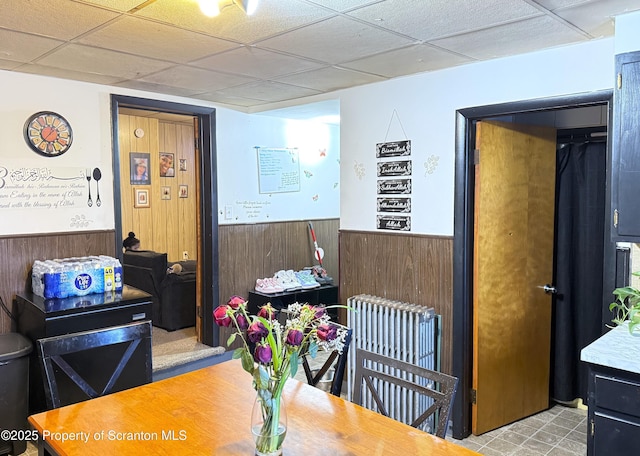 dining space featuring a paneled ceiling, wood walls, and radiator heating unit