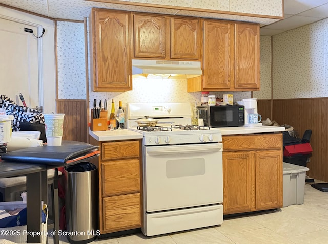 kitchen featuring light tile patterned floors, gas range gas stove, and wood walls