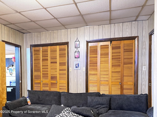 unfurnished living room featuring a paneled ceiling and wooden walls