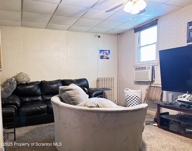 carpeted living room featuring radiator, ceiling fan, and a drop ceiling