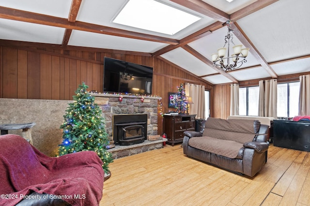 living room with vaulted ceiling with skylight, wood-type flooring, a chandelier, a wood stove, and wood walls